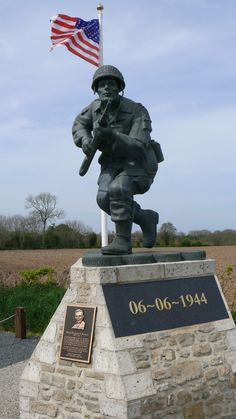 a statue of a soldier with an american flag flying in the sky behind it and another memorial sign