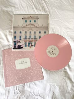 a pink record sitting on top of a bed next to an envelope and cd case