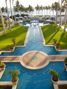 an outdoor swimming pool surrounded by palm trees and lawns with water running through it