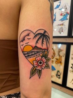 a woman's arm with a heart shaped tattoo on it and flowers in the foreground