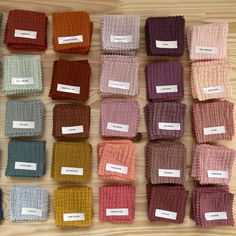 many different colors of knitted cloths on a table with labels attached to them