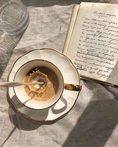 an open book and a cup of coffee on a table with a spoon in it