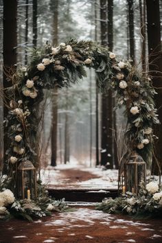 an outdoor wedding arch decorated with greenery and white flowers in the snow, surrounded by pine trees