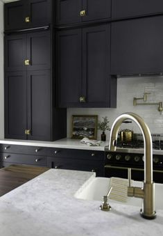 a kitchen with black cabinets and white counter tops, gold pulls on the faucet