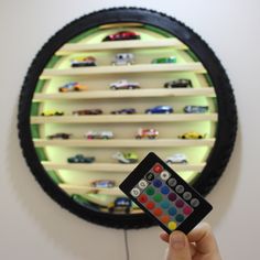 a person holding a remote control in front of a wall mounted toy car display