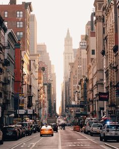 a busy city street with tall buildings and cars parked on the side of the road