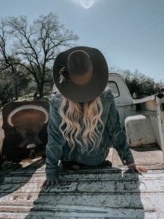 a woman sitting on the back of a truck wearing a black hat and denim jacket