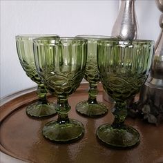 three green glass goblets sitting on top of a table next to a vase