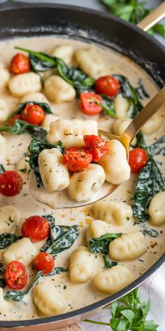 a pan filled with ravioli and spinach covered in cheese, tomatoes and herbs