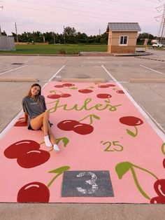 a woman sitting on the ground in front of a pink rug with cherries painted on it