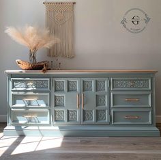 an old dresser is painted blue and has gold hardware on the doors, with a decorative wall hanging above it