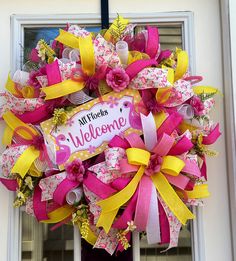 a pink and yellow welcome wreath hanging on the front door of a house with ribbon around it