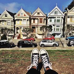 someone's feet are standing on the ground in front of some houses and parked cars