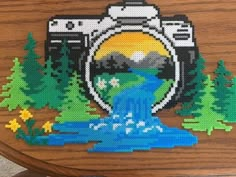 a cross - stitch picture of a camera with water running through it and mountains in the background