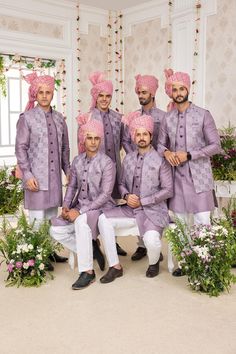 a group of men dressed in purple outfits posing for a photo with flowers on the wall behind them