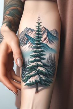 a woman's arm with a pine tree tattoo on it and mountains in the background