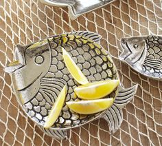 two fish shaped plates with lemon wedges on the side and silver serving utensils