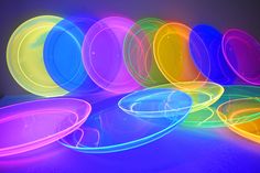 neon colored plastic plates are arranged in a row on a table with black light coming from the top