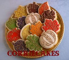 decorated cookies in the shape of autumn leaves and acorns on a gold plate