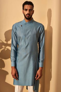 Editor's Note This set features a mineral blue color asymmetric paneled kurta paired with cream pant cut pyjama. Color: Mineral Blue Fabric: Cotton Silk; Terricotton Care: Dry Clean Only About the Designer The Dhruv Vaish Label is a menswear label specializing in Indian and Western Wear, with an exhaustive portfolio of Bespoke Tailoring. Kurta Designs Men's, Cream Pant, Stylish Boy Clothes, Mens Traditional Wear, Boys Kurta Design, Wedding Kurta For Men, Indian Groom Wear, Gents Kurta Design, Gents Kurta