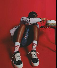 a woman sitting on the floor with her legs crossed, wearing sneakers and eating cake