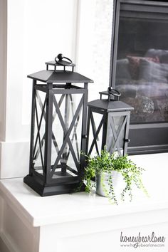 two black lanterns sitting on top of a white table next to a potted plant