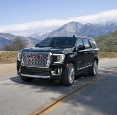 a black suv driving down the road with mountains in the background