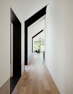 an empty hallway with wooden floors and black trim on the walls, leading to another room