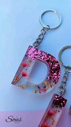 the letter d is made out of paper and has pink flowers on it, along with two silver metal key chains