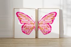 two pink and gold butterfly paintings in front of a white wall with wood flooring