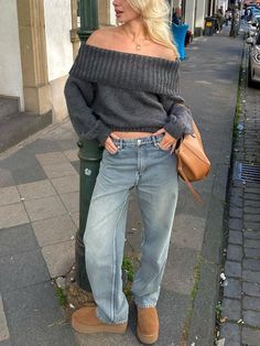 a woman standing next to a pole on the side of a road wearing jeans and a sweater