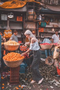 a woman standing in front of a market filled with oranges and other fruit items