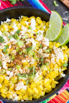 mexican corn salad in a black bowl with lime wedges and cilantro on the side