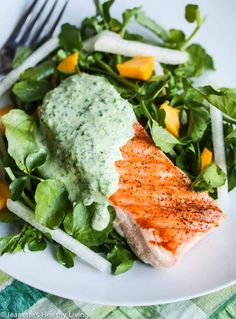 a white plate topped with salmon and greens next to a fork on top of a table