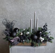 an arrangement of candles, ornaments and greenery is displayed on a wooden block in front of a wall