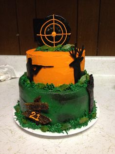 a three tiered cake is decorated with green and orange frosting, black decorations and trees