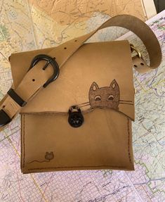 Adorable Cat and mouse on light brown leather purse. This bag is 9x8 with a 16 inch strap. The Phone pouch and the card pocket are plaid print on leather.  My bags are inspired by the Swiss Army Knife, made to last a lifetime with useful features. I like distressed leather and rugged edges. I feel it gives my pieces their own personality. All items are 100% made by me, from design to all the hand sewing (saddle stitch) .Each bag takes about 8 hours of work time. Cat Design Pouch Shoulder Bag For Travel, Travel Pouch Shoulder Bag With Cat Design, Daily Use Crossbody Bag With Cat Design, Travel Shoulder Bag With Cat Design, Cat Design Crossbody Shoulder Bag For Everyday Use, Everyday Use Crossbody Shoulder Bag With Cat Design, Leather Shoulder Bag With Removable Pouch For Personal Use, Everyday Crossbody Shoulder Bag With Cat Design, Cat Design Shoulder Satchel