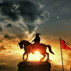 a statue of a man riding on the back of a horse next to a red flag