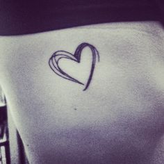 a small heart tattoo on the back of a woman's left side ribcage