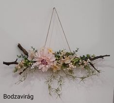 a flower arrangement hanging from a wall with branches and flowers on it's sides