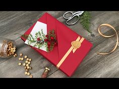 an open red envelope with gold ribbon and flowers on it next to scissors, sprig of greenery