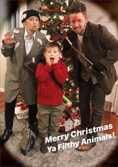 two men and a boy standing in front of a christmas tree with the words merry christmas ya filthy animals