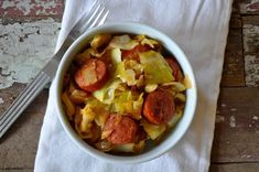 a white bowl filled with cabbage and sausage next to a fork on top of a napkin