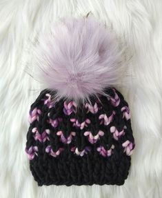 a knitted hat with a pom - pom on top sitting on white fur