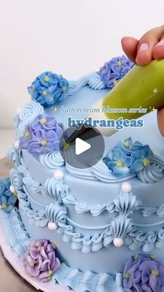 someone is cutting into a blue cake with purple flowers on the bottom and green icing