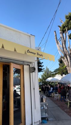 people are sitting at tables under umbrellas outside the building with white and yellow awnings