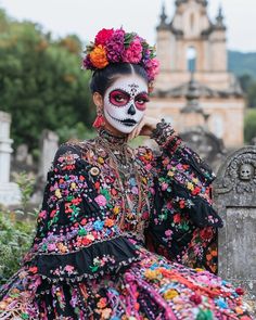 a woman with face paint and flowers on her head sitting in front of a grave