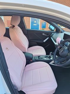 the interior of a white car with pink leather seats and steering wheel, in front of a brick building