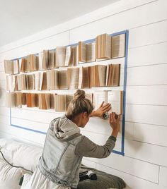 a woman is sitting on a bed and looking at books hanging on the wall behind her