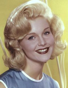 an old photo of a woman with blonde hair and blue shirt smiling at the camera